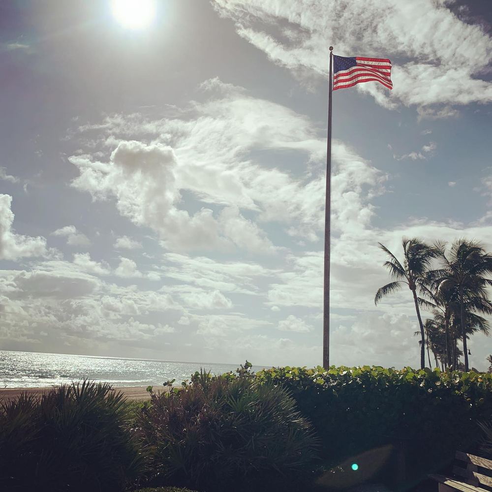 American flag above the ocean, palms and sunlit clouds on Palm Beach Island.